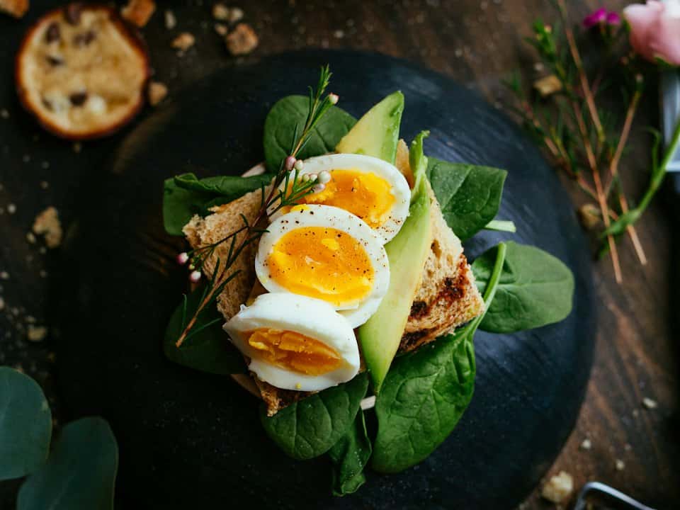 Felie de pâine prăjită cu ouă fierte tăiate în jumătăți, felii de avocado și frunze de spanac