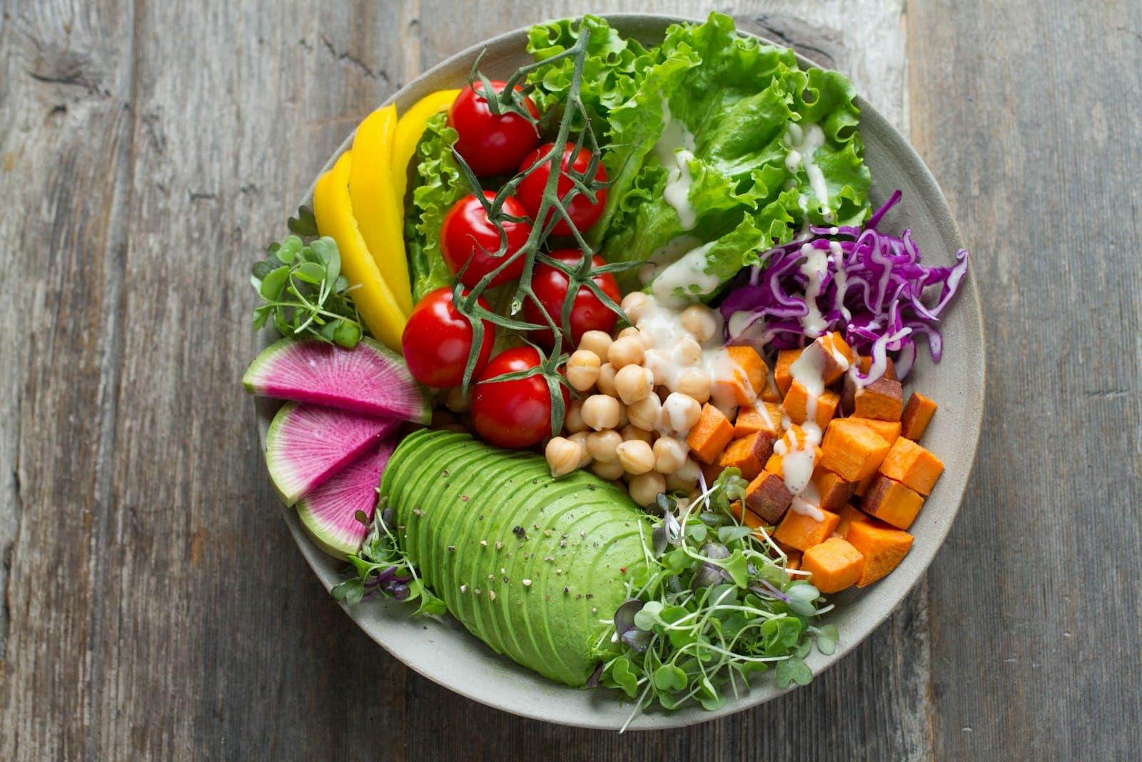 Bol cu salată verde, roșii cherry, năut, avocado și cuburi de cartof dulce, văzut de sus